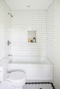 a white toilet sitting next to a bath tub in a bathroom with black and white tiles on the floor