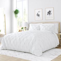 a white bed in a bedroom next to a window with potted plants on the side