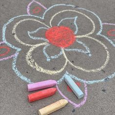 three crayons are laying on the ground next to a flower drawn in chalk