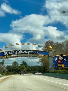 the entrance to walt world with flags flying in the wind and cars driving down the road