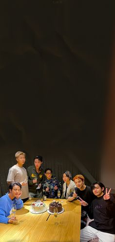 a group of people sitting around a wooden table with a cake on top of it