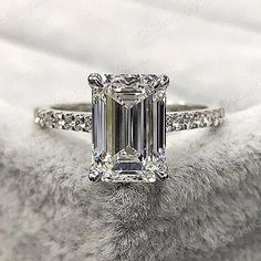 an emerald - cut diamond ring sits on a white blanket