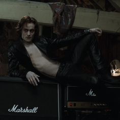 a shirtless man sitting on top of two amps