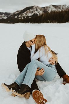 a man and woman sitting in the snow kissing