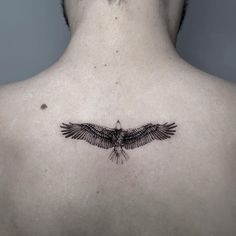 the back of a man's neck with a black bird tattoo on his chest