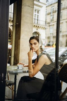 a woman sitting at a table in front of a window talking on her cell phone