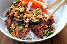 a white bowl filled with meat and veggies on top of rice next to chopsticks