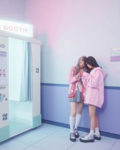 two young women standing next to each other in front of a wall with an advertisement on it