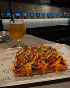 a pizza sitting on top of a white plate next to a glass of beer at a bar