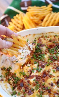 a hand dipping some fries into a bowl of cheesy potato casserole