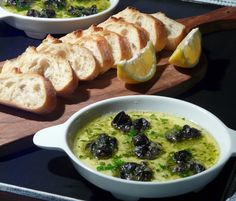 a bowl of soup with bread and olives on a cutting board next to it