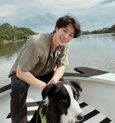 a man petting a dog on the bow of a boat with trees in the background