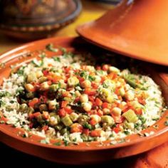 a bowl filled with rice and vegetables on top of a wooden table next to an orange plate