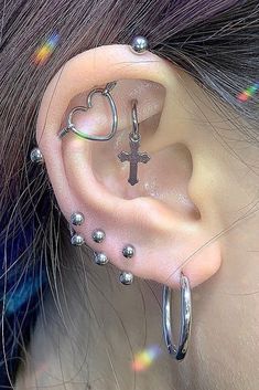 a woman with piercings on her ear wearing a cross and heart shaped hoop earrings