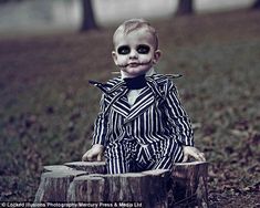 a young boy dressed as a skeleton sitting on top of a tree stump