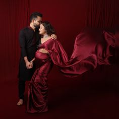 a man and woman standing next to each other in front of a red curtain with their arms around each other