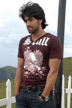 a man standing next to a white fence with his hands in his pockets and looking at the camera