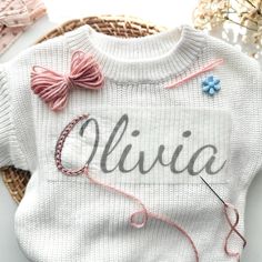 a white sweater with the word alvia on it and some knitting needles next to it