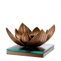 a bronze flower sculpture sitting on top of a glass block in front of a white background