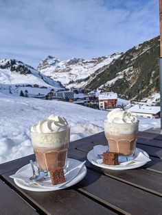 two ice cream sundaes sitting on top of a wooden table covered in snow