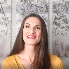 a woman with long hair is smiling and looking at the camera while wearing a yellow shirt