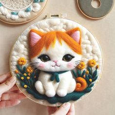 a hand is holding a small embroidery kit with an orange and white cat on it