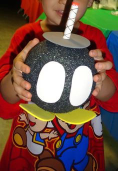 a young boy holding up a black object with white circles on it's face