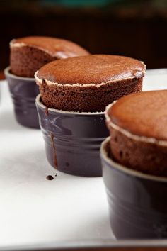 three chocolate cakes sitting in black cups on a table