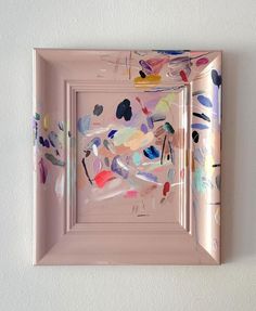 an abstract painting on a white wall in a pink frame with paint splattered over it