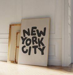 a new york city sign sitting on top of a wooden floor next to two framed pictures