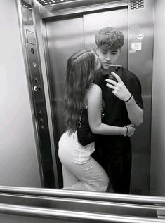 a young man and woman standing in front of an elevator looking at their cell phones