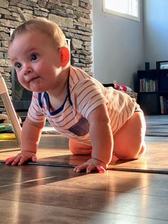 a baby crawls on the floor in front of a computer monitor and looks at the camera