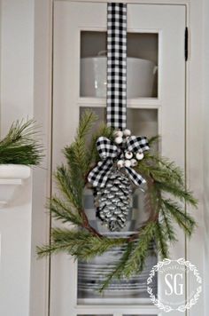 a pine cone wreath is hung on the front door's hutch, decorated with plaid ribbon and pine cones