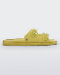 Side view of a yellow Melissa Wide Slide with two straps fastened on top with two clear buckles and a "m" logo on the side. Trendy Slides With Buckle Closure And Round Toe, Trendy Jelly Slide Sandals With Buckle Closure, Modern Slides With Buckle Closure For Beach, Modern Beach Slides With Buckle Closure, Trendy Yellow Sandals With Buckle Closure, Modern Double Strap Slides With Buckle Closure, Spring Jelly Slide Sandals With Buckle, Trendy Summer Slides With Double Strap, Famous Fashion