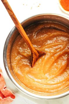 a wooden spoon in a metal bowl filled with orange colored sauce and seasoning flakes