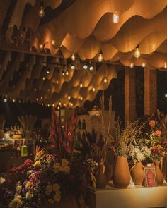 an arrangement of flowers in vases on a table with lights hanging from the ceiling