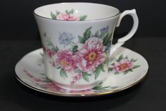 a tea cup and saucer with pink flowers on the side, sitting on a black surface