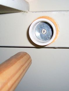 a close up of a wooden handle on a white cabinet door with a hole in it