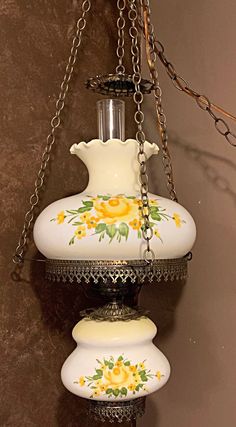 a white vase with yellow flowers painted on it hanging from a chain attached to a wall