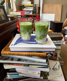 two glasses filled with green liquid sitting on top of books