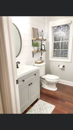 a white toilet sitting next to a sink in a bathroom under a window with wooden floors