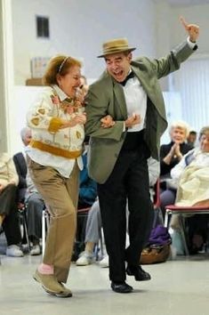 two people dancing in front of an audience with their arms out and one person wearing a hat