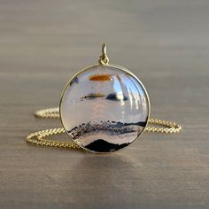 This peaceful disc brings to mind a horizon in miniature, cut, polished, and set in its snug golden bezel by artist Mimi Favre 18k yellow gold Montana agate 27mm (1 1/16") in diameter1.3mm chain is 18" long Modern Round Cabochon Necklace, Modern Cabochon Necklace, Round Agate Jewelry For Meditation, Artistic Gold Round Jewelry, Minimalist Round Cabochon Necklace, Minimalist Round Cabochon Necklaces, Unique Round Pendant Necklace With Polished Finish, Modern Cabochon Necklaces For Gifts, 14k Gold Round Keepsake Necklace