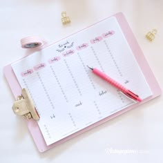 a pink clipboard with a calendar and pen on it next to some gold clips