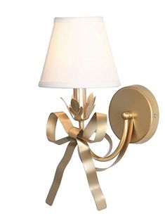 a wall light with a white shade on it and a gold ribbon around the lamp