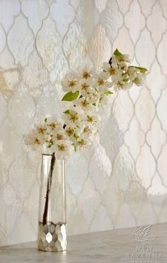 a silver vase with white flowers in it on a table next to a wallpaper