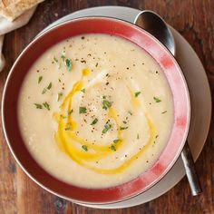 a red bowl filled with soup on top of a wooden table next to a piece of bread