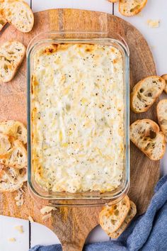 a casserole dish filled with cheese and bread on a cutting board next to blue napkin