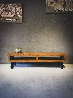 a large wooden bench sitting in front of two paintings on the wall and one has a vase with flowers on it