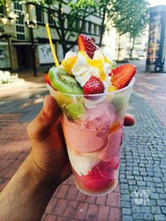 a person holding up a cup filled with ice cream and fruit